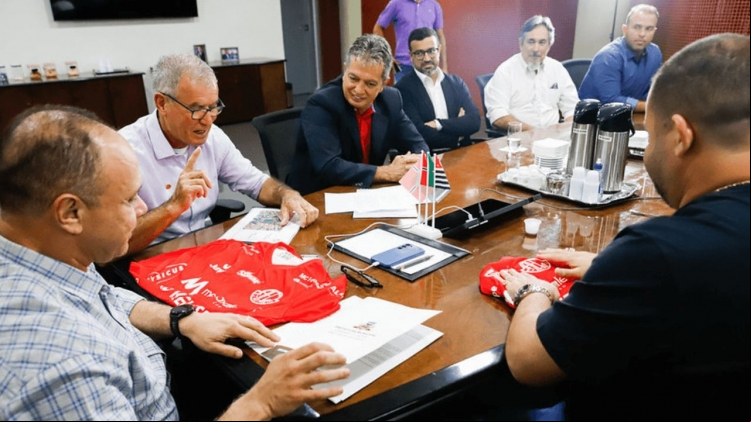 Prefeito Fábio Candido recebe a camisa oficial do América Futebol Clube durante reunião com a diretoria do clube e o secretário de Esportes. Parceria visa fortalecer o esporte em Rio Preto.
